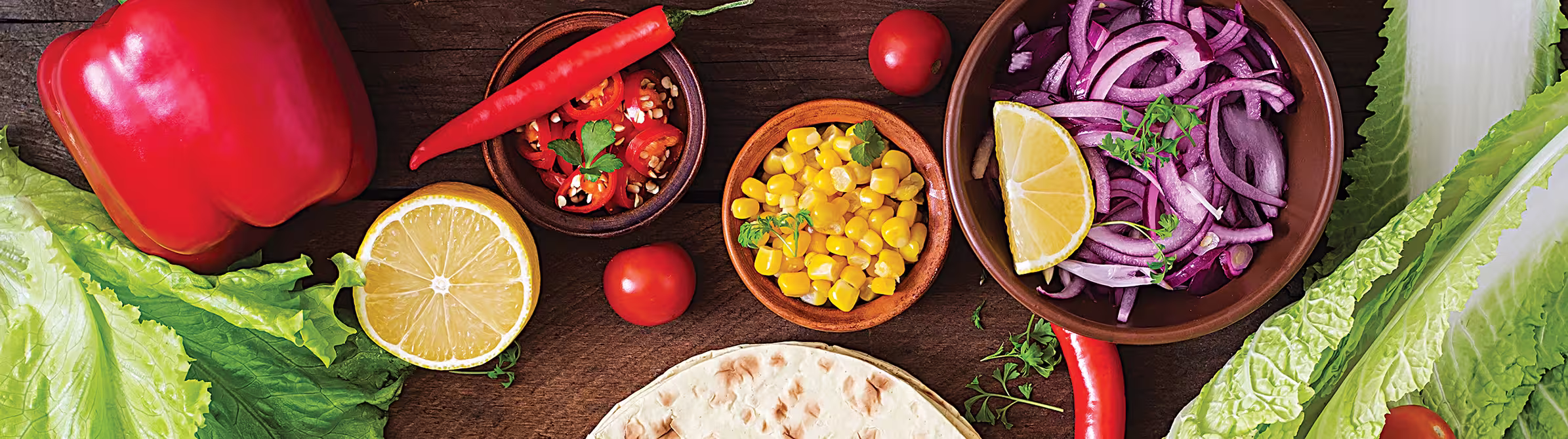 A table with bowls of vegetables and fresh ingredients, including peppers, onions, and lettuce